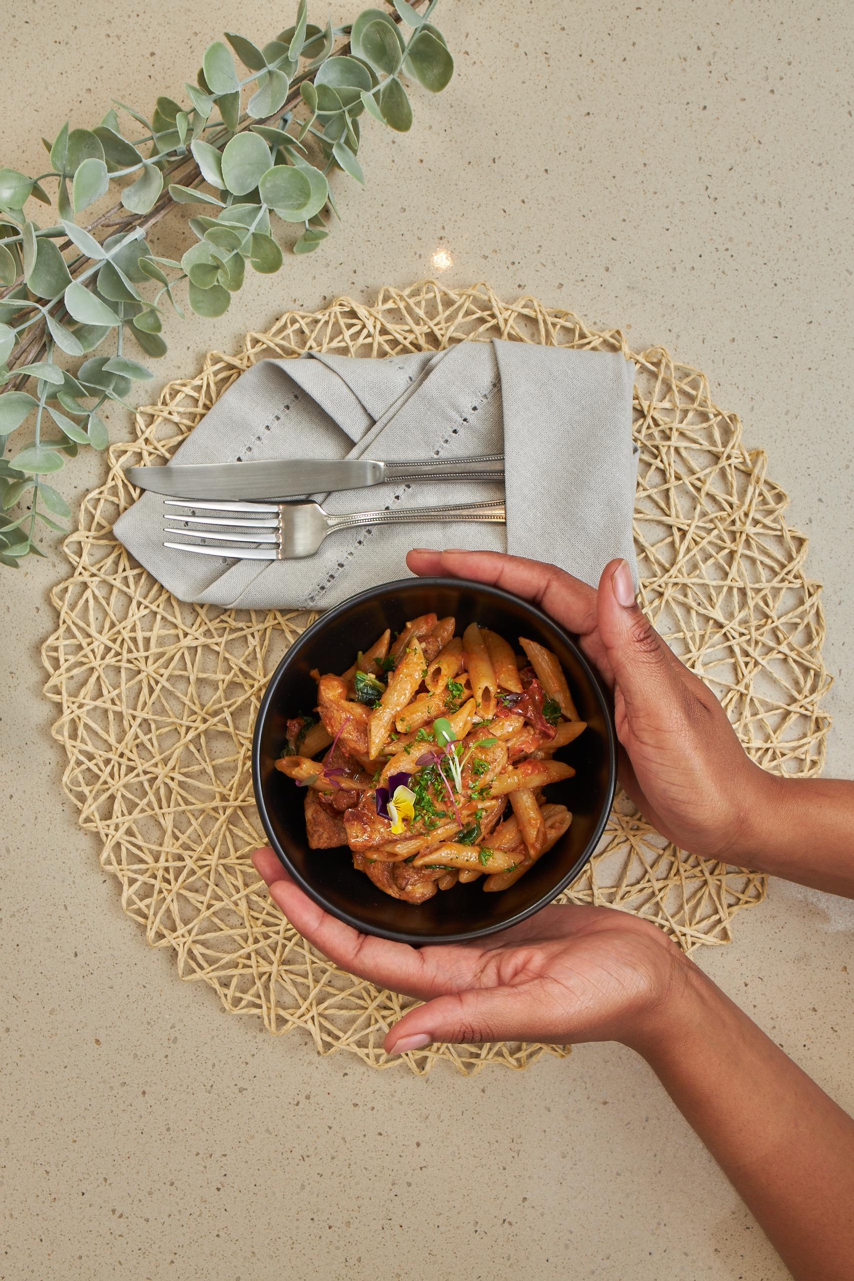 Close-up of hands holding a fresh pasta bowl from Nutridish - healthy, hearty, ready-to-eat comfort food.